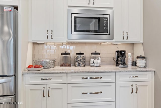 kitchen with backsplash, white cabinetry, light stone countertops, and stainless steel appliances