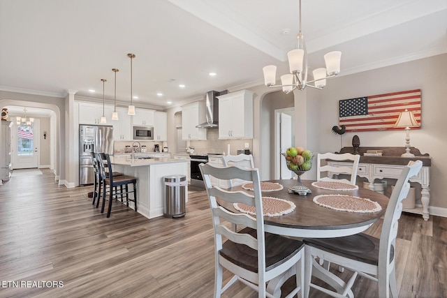 dining area with arched walkways, light wood finished floors, an inviting chandelier, and crown molding