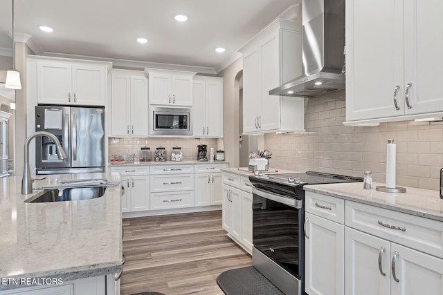 kitchen featuring white cabinets, light wood-style floors, wall chimney exhaust hood, stainless steel appliances, and a sink
