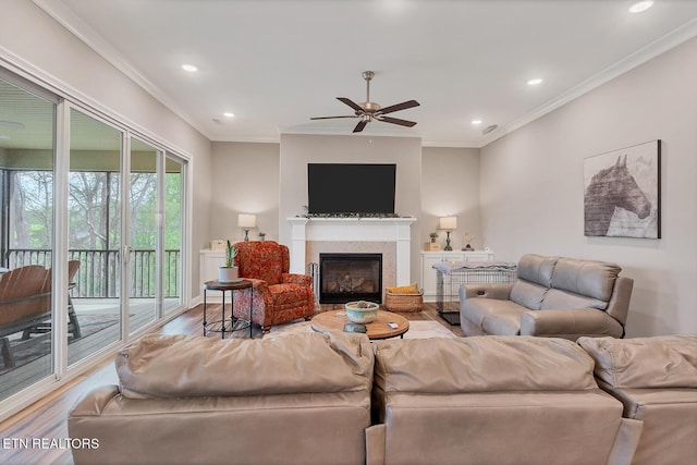 living area with a ceiling fan, crown molding, recessed lighting, wood finished floors, and a glass covered fireplace