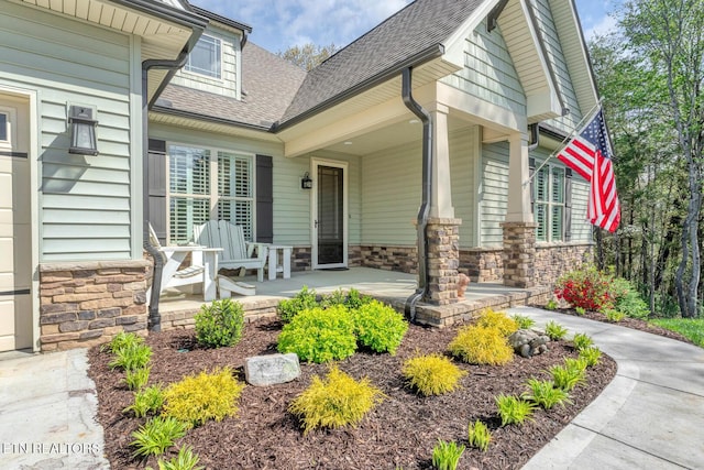 property entrance with roof with shingles, stone siding, and covered porch