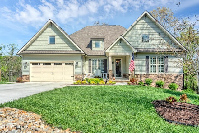 craftsman-style home featuring a front yard, stone siding, a garage, driveway, and roof with shingles