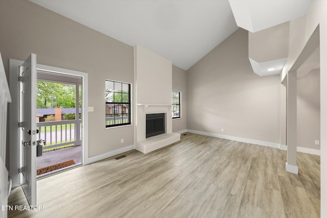 unfurnished living room featuring plenty of natural light, light wood-style flooring, baseboards, and high vaulted ceiling