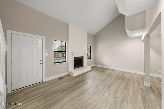 unfurnished living room with light wood finished floors, high vaulted ceiling, a brick fireplace, visible vents, and baseboards