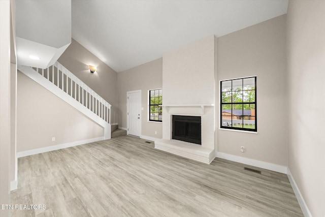unfurnished living room featuring baseboards, visible vents, stairs, high vaulted ceiling, and wood finished floors