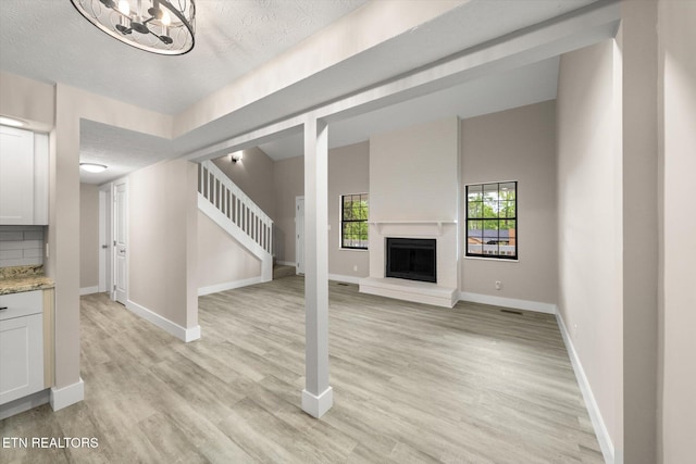 unfurnished living room featuring light wood-type flooring, baseboards, a fireplace with raised hearth, and stairs