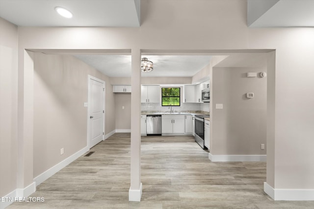 kitchen with a sink, light countertops, white cabinets, baseboards, and appliances with stainless steel finishes