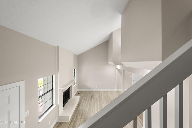unfurnished living room featuring baseboards, lofted ceiling, light wood finished floors, and a fireplace with raised hearth