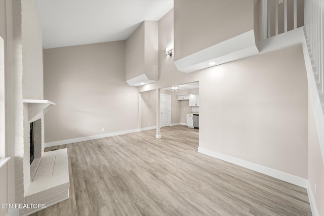 unfurnished living room with light wood finished floors, a fireplace, baseboards, and a high ceiling