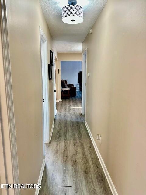 hall featuring baseboards, a textured ceiling, and wood finished floors