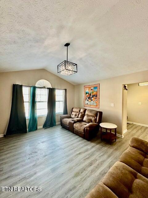 living area with a notable chandelier, baseboards, light wood-type flooring, a textured ceiling, and lofted ceiling