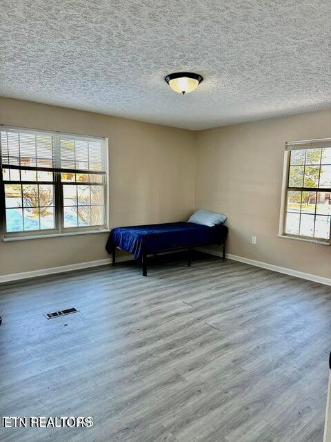 unfurnished bedroom featuring visible vents, baseboards, wood finished floors, and a textured ceiling