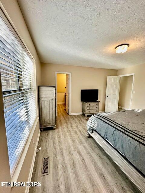 bedroom featuring visible vents, baseboards, light wood-style floors, and a textured ceiling