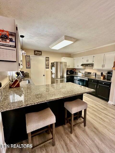 kitchen with a kitchen bar, a peninsula, dark stone countertops, a sink, and stainless steel appliances