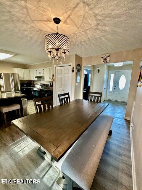 unfurnished dining area featuring a textured ceiling, wood finished floors, a notable chandelier, and baseboards