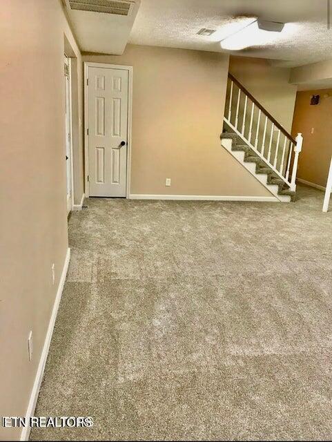 carpeted empty room with visible vents, baseboards, stairway, and a textured ceiling