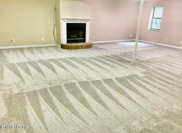 unfurnished living room with carpet, a fireplace with raised hearth, and baseboards