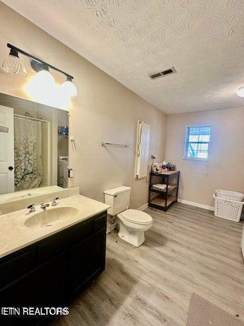 bathroom with vanity, vaulted ceiling, visible vents, toilet, and wood finished floors