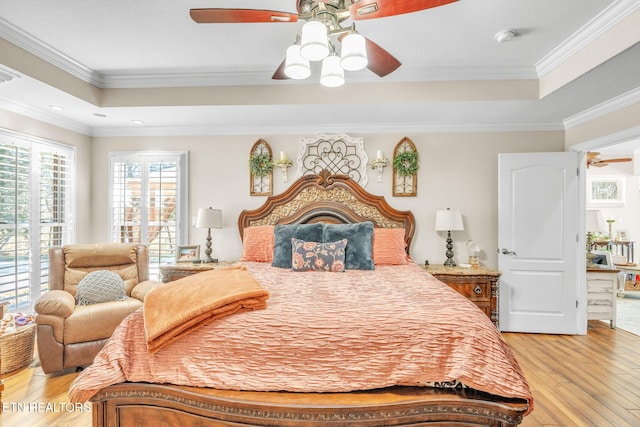 bedroom featuring light wood-style flooring, a raised ceiling, ceiling fan, and crown molding