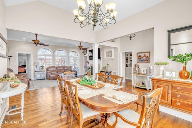 dining space with decorative columns, high vaulted ceiling, light wood-style flooring, and ceiling fan with notable chandelier