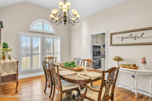 dining space featuring light wood-style flooring, a notable chandelier, baseboards, and lofted ceiling