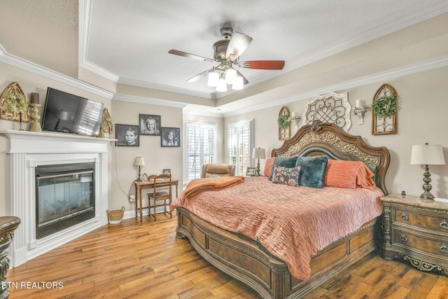 bedroom with a raised ceiling, ornamental molding, a glass covered fireplace, and hardwood / wood-style flooring