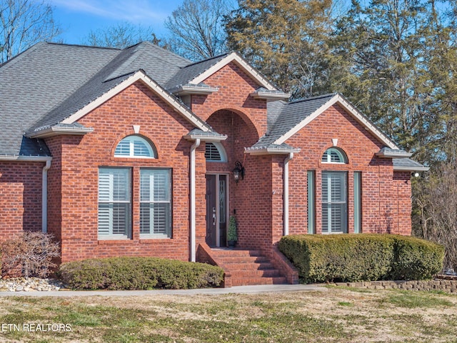 traditional home with a shingled roof, a front lawn, and brick siding