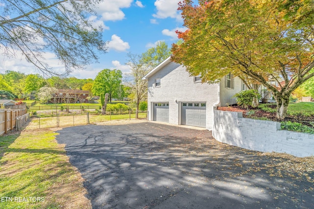 view of side of property featuring fence, stucco siding, a garage, and aphalt driveway