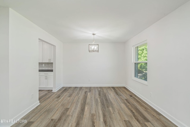 unfurnished dining area with baseboards, a notable chandelier, and light wood-style floors