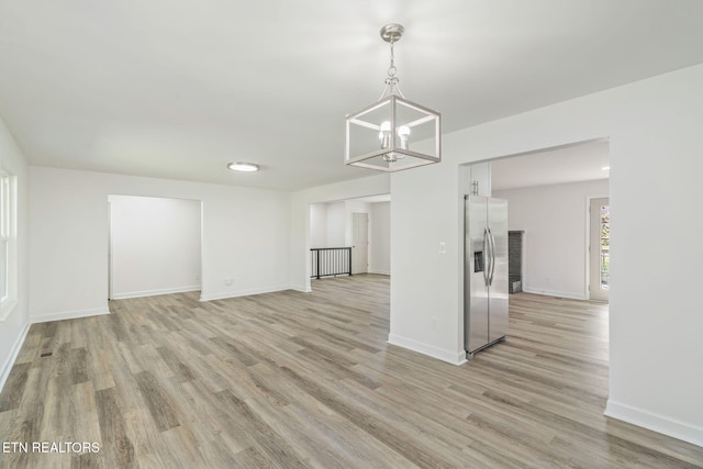unfurnished living room with baseboards, light wood-type flooring, and an inviting chandelier