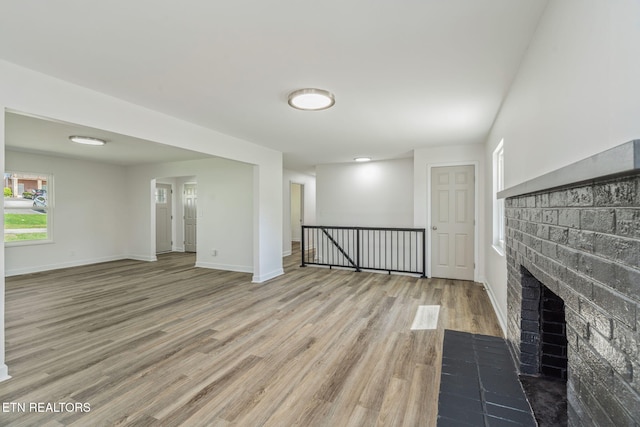 unfurnished living room featuring a brick fireplace, baseboards, and wood finished floors
