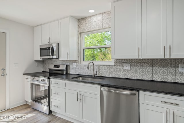 kitchen with tasteful backsplash, white cabinetry, light wood-style floors, appliances with stainless steel finishes, and a sink