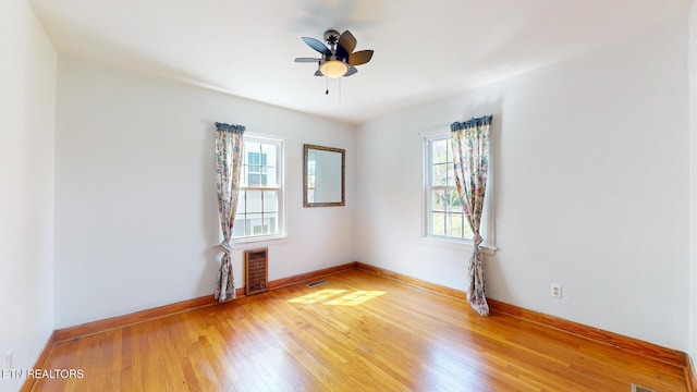 unfurnished room with a ceiling fan, heating unit, light wood-style floors, baseboards, and visible vents