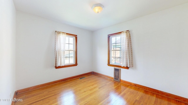 spare room with wood finished floors, visible vents, and baseboards