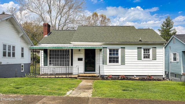 view of front of property featuring a chimney, a front lawn, and roof with shingles