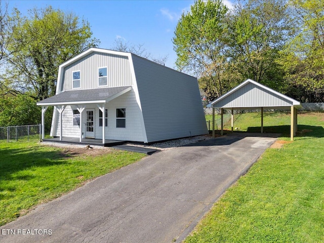 view of front facade with a carport, a porch, a front lawn, a gambrel roof, and driveway