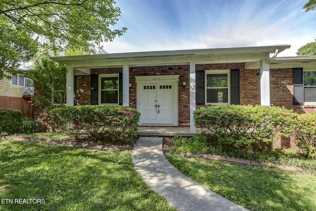 view of front of property with covered porch, a front lawn, and brick siding