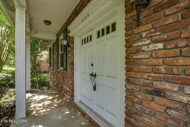 doorway to property featuring a porch and brick siding