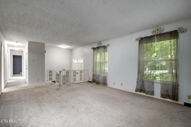 carpeted spare room with a healthy amount of sunlight, baseboards, and a textured ceiling