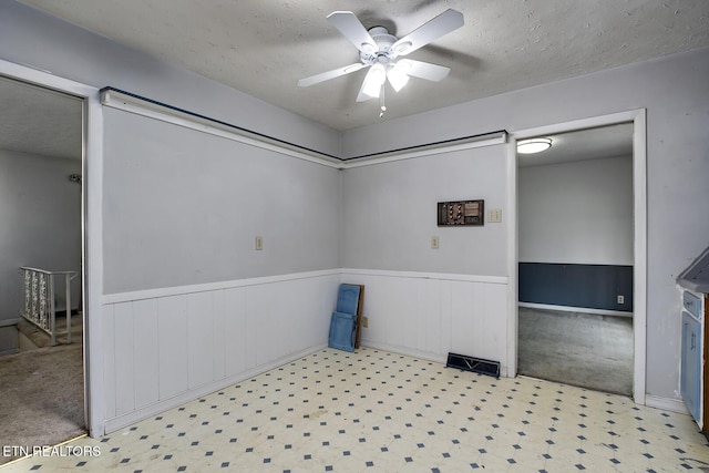 unfurnished room featuring a textured ceiling, ceiling fan, and a wainscoted wall