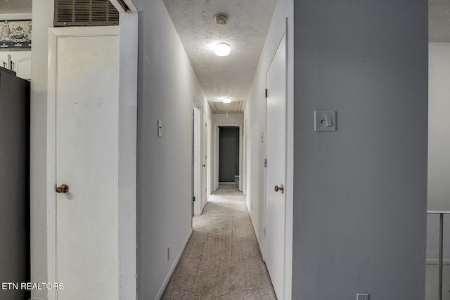 hallway featuring visible vents, light carpet, baseboards, attic access, and a textured ceiling