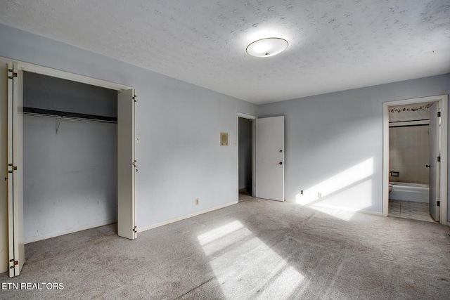 unfurnished bedroom featuring a textured ceiling, baseboards, carpet, and ensuite bath