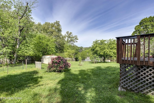 view of yard featuring fence, a storage unit, a wooden deck, and an outbuilding