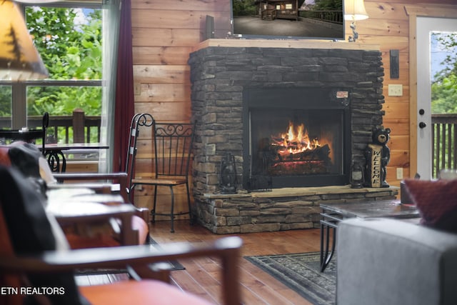 living area featuring hardwood / wood-style floors, a stone fireplace, and wood walls