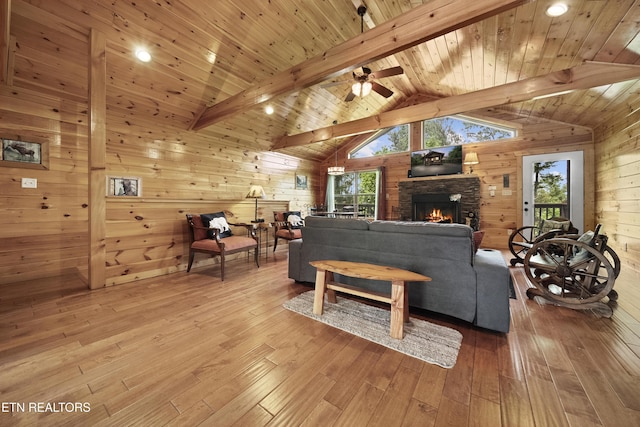 living room featuring wooden ceiling, wood-type flooring, vaulted ceiling with beams, wooden walls, and a stone fireplace