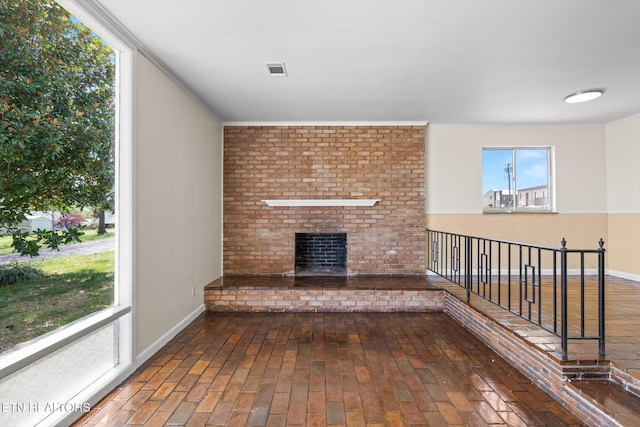 unfurnished living room with visible vents, baseboards, a brick fireplace, ornamental molding, and brick floor