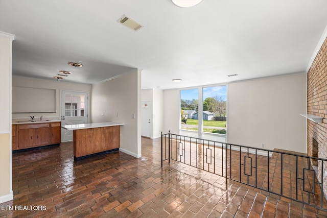 kitchen with a peninsula, light countertops, visible vents, brick floor, and a sink