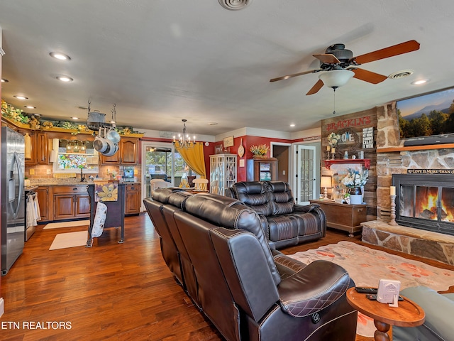 living area with visible vents, a stone fireplace, recessed lighting, ceiling fan with notable chandelier, and dark wood-type flooring
