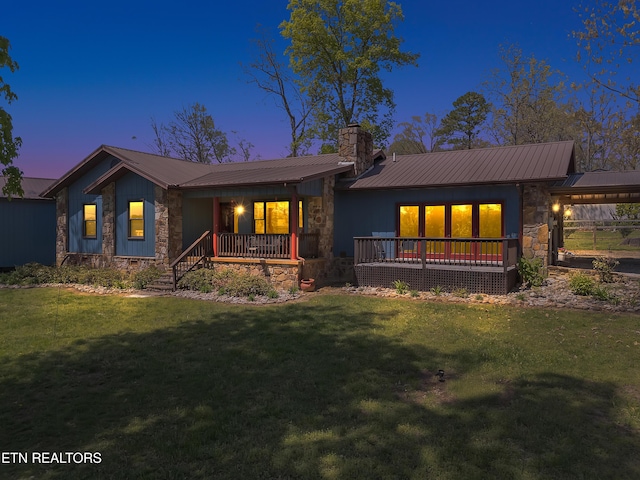 back of house featuring metal roof, stone siding, and a lawn