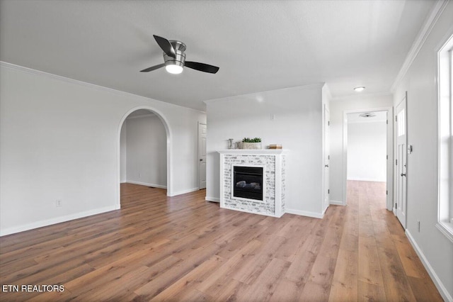 unfurnished living room featuring a tiled fireplace, ornamental molding, a ceiling fan, and light wood-style floors